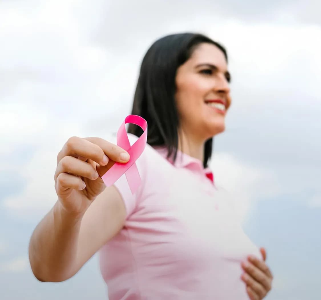 Smiling woman holding a pink awareness ribbon against the sky