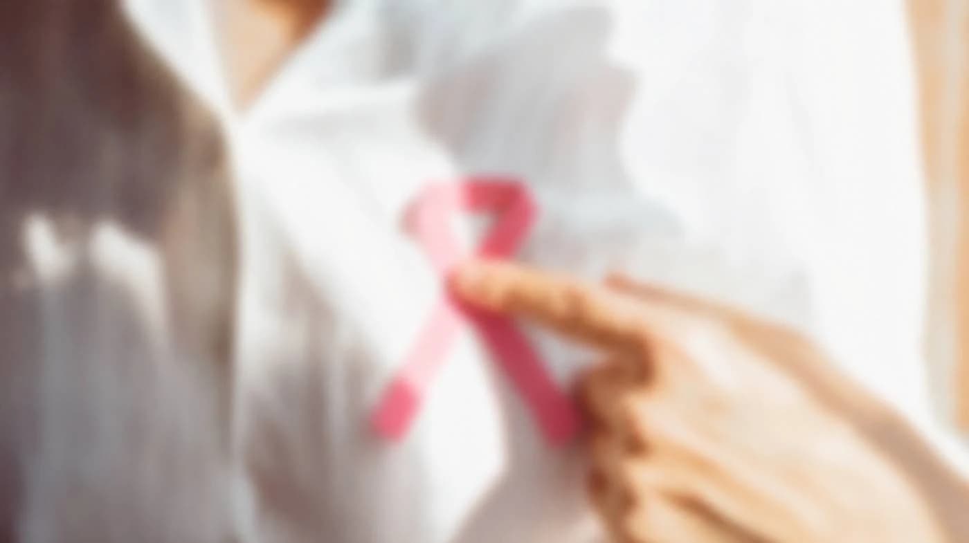 Blurred photo of a hand holding a pink awareness ribbon